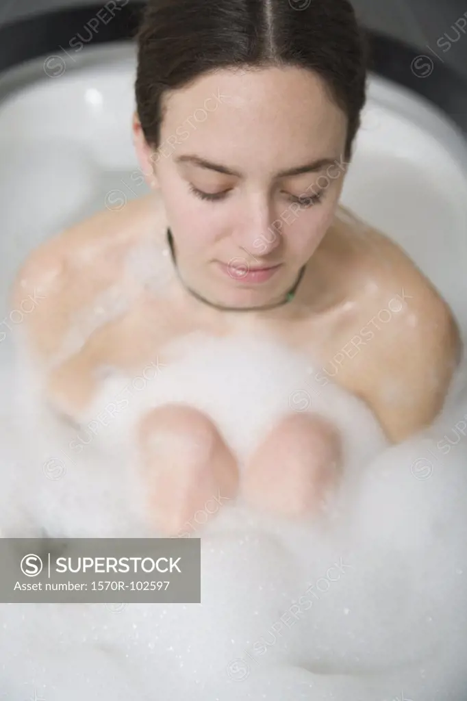 Woman with brown hair sitting in bath hugging knees