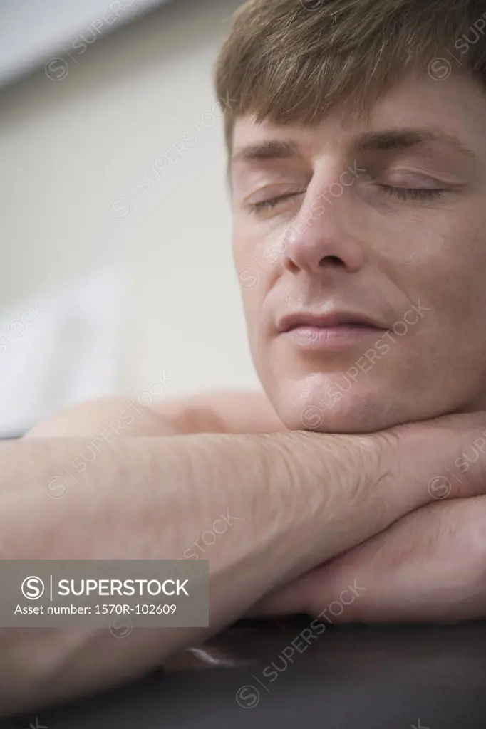 Man with eyes closed resting his head on hands at the edge of bathtub
