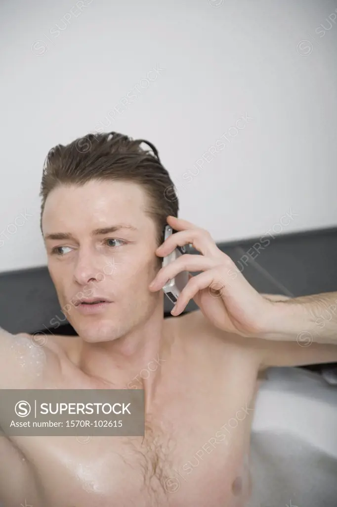 Man sitting in a bathtub and holding a mobile phone