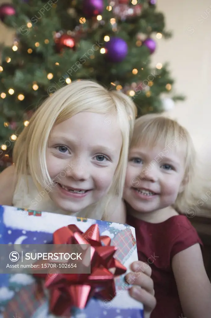 Two young girls holding present near Christmas tree