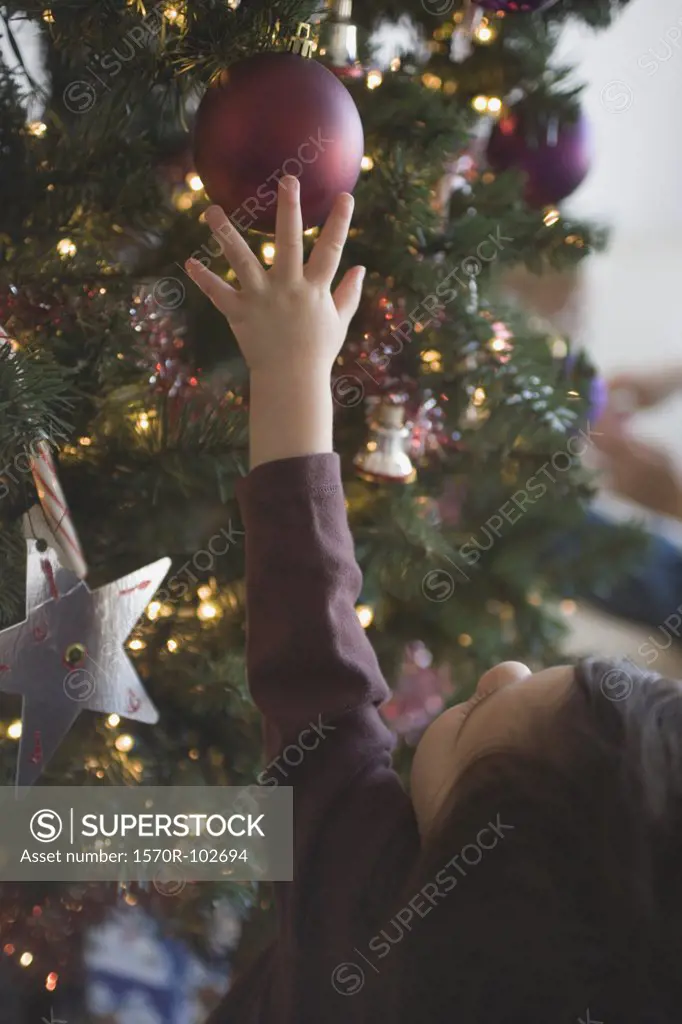 Young girl reaching for bauble on Christmas tree