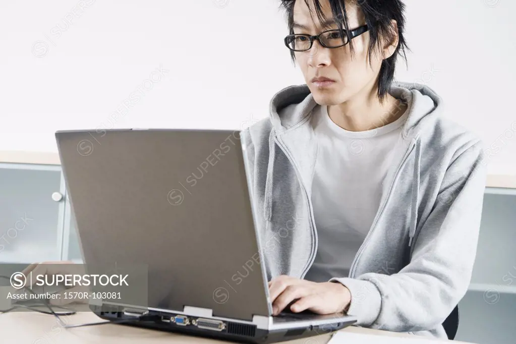 An Asian man working on a laptop in an office setting