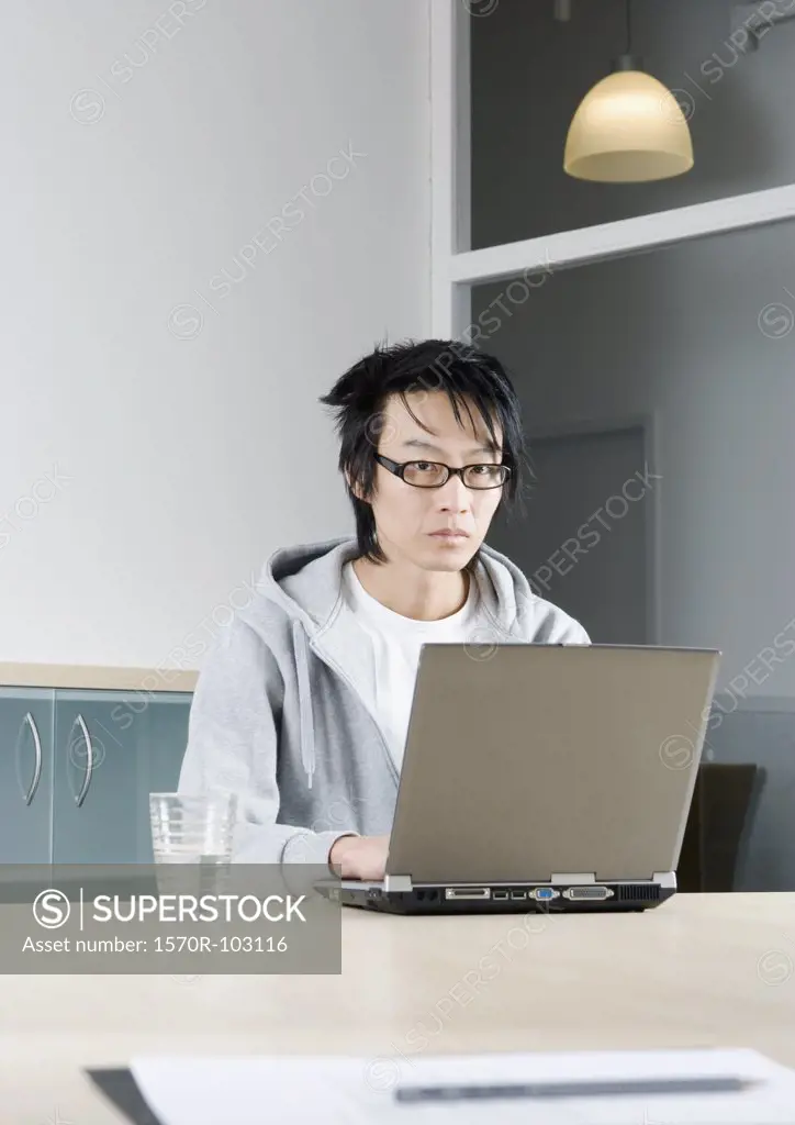 An Asian man working on a laptop in a conference room
