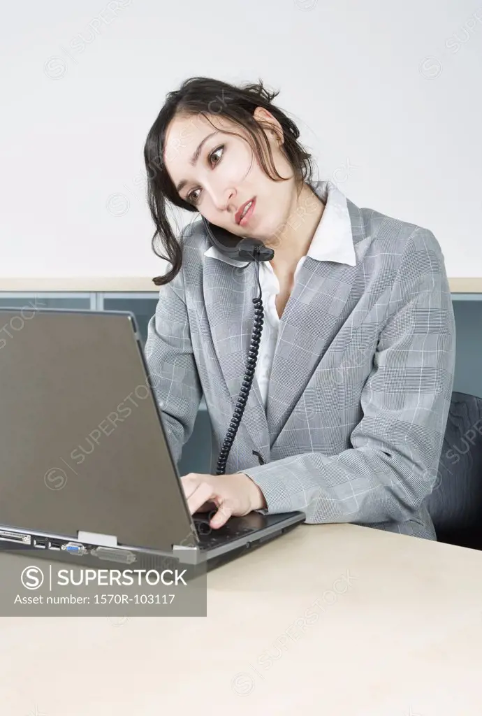 A woman working on a laptop while talking on the telephone