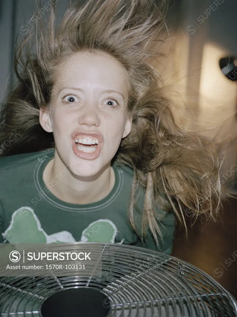 A woman making a crazy face above a fan