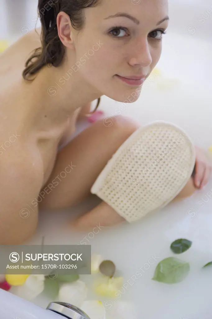 Young woman sitting in bath with loofah