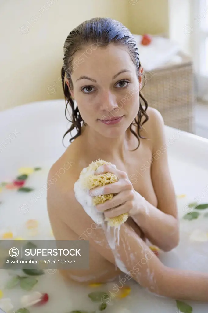 Young woman sitting in bathtub holding sponge