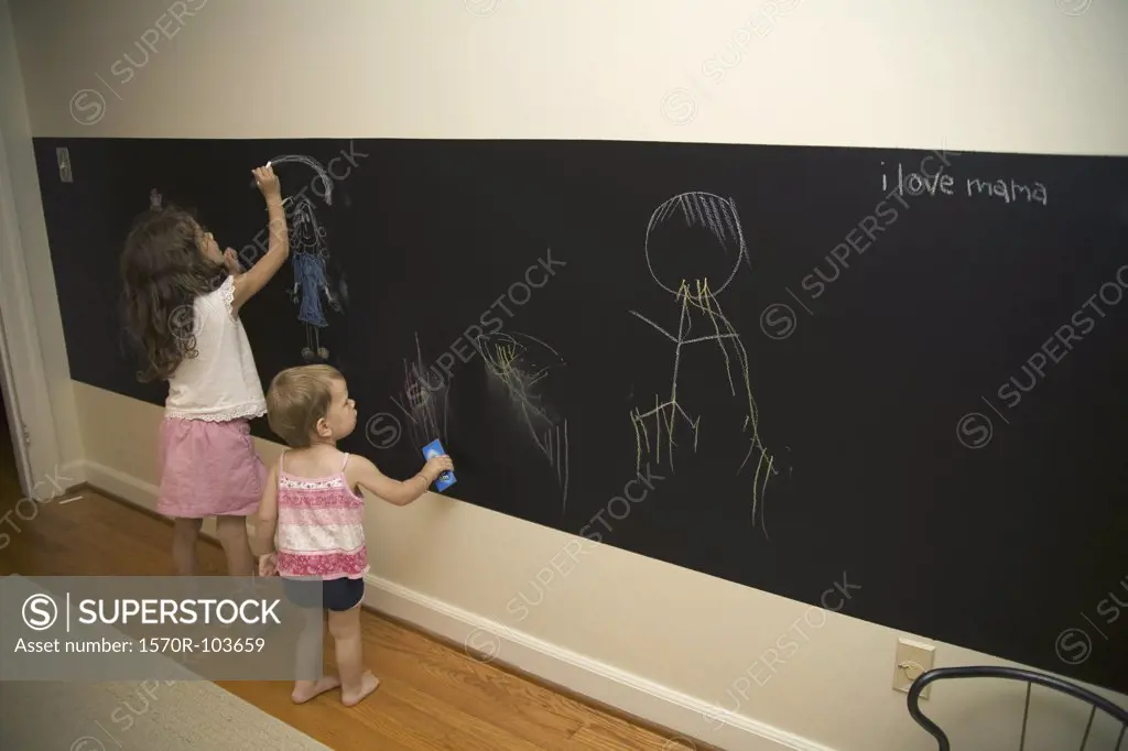 Two young girls drawing on blackboard