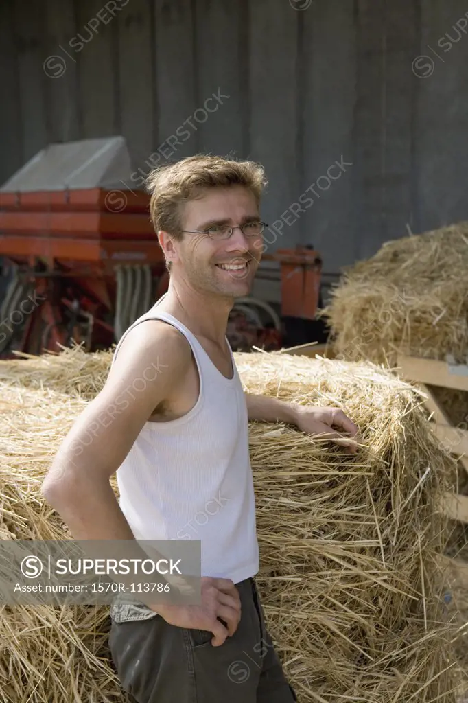 Farm worker resting next to bale of hay and smiling