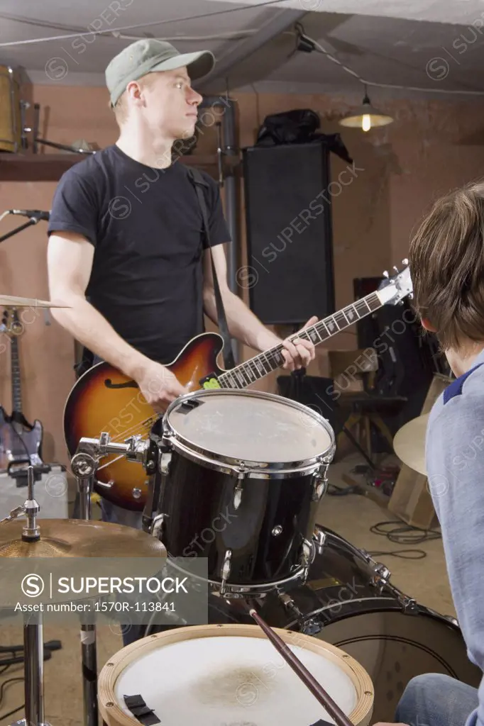 Two men practicing the drums and guitar