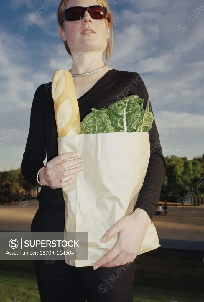 Woman standing in a park and holding a bag of groceries