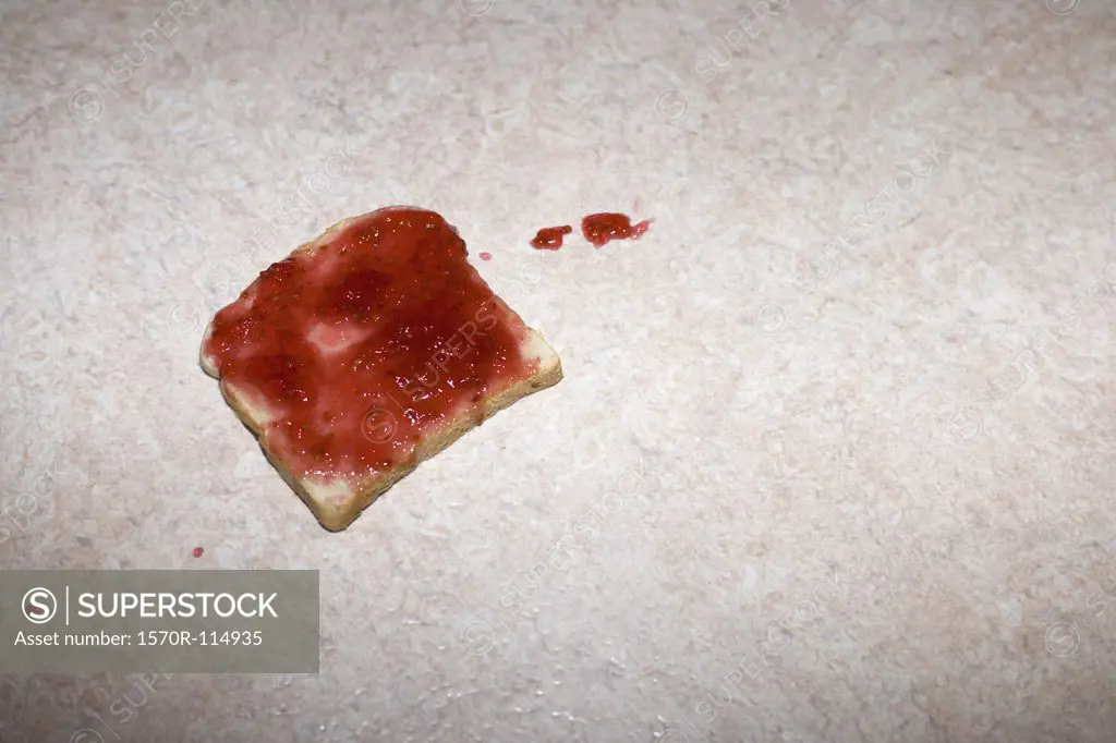 Slice of toast with strawberry jam dropped on the floor