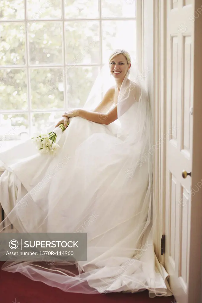 Bride sitting by window and holding wedding bouquet