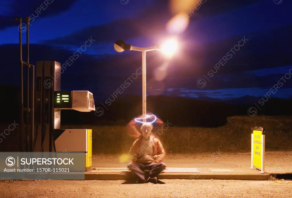 Young man sitting on floor of gas station with halo shape above his head
