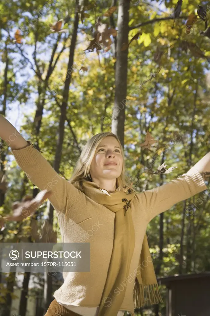 Woman raising her arms and leaves falling from trees