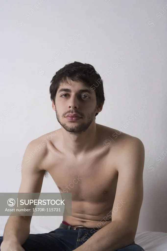Young man sitting shirtless on bed