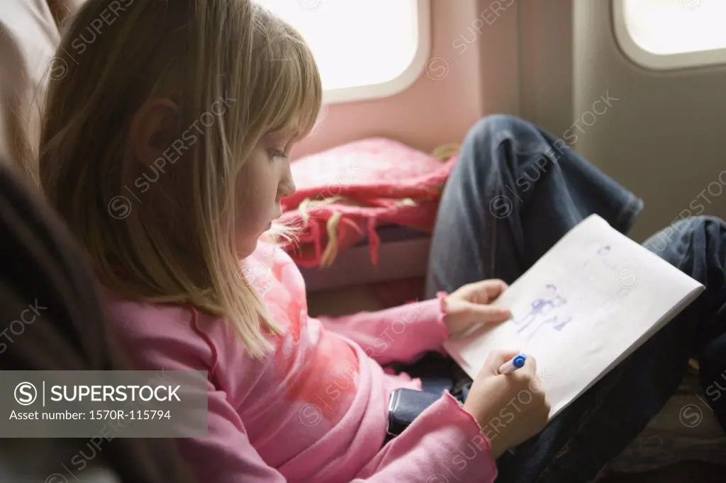 Young girl sitting in an airplane and drawing in a sketch pad