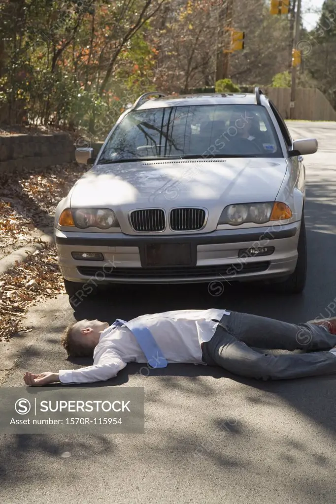 Man lying down on a road in front of a car
