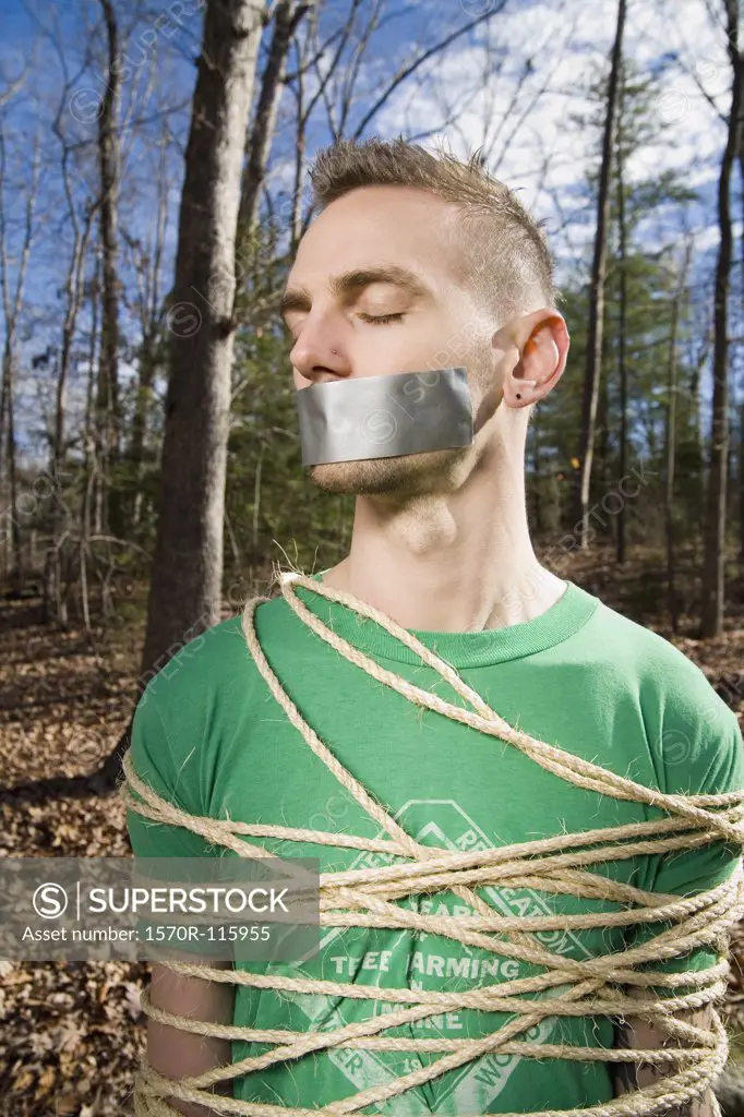 Man standing in the woods bound in rope and with adhesive tape covering his mouth