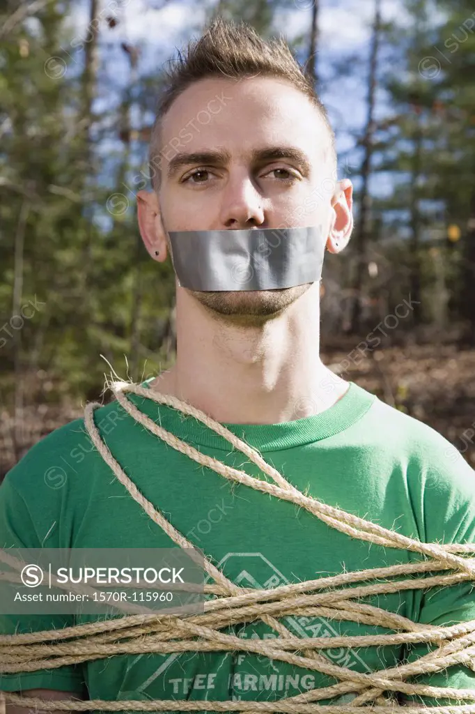 Man standing in the woods bound in rope and with adhesive tape covering his mouth