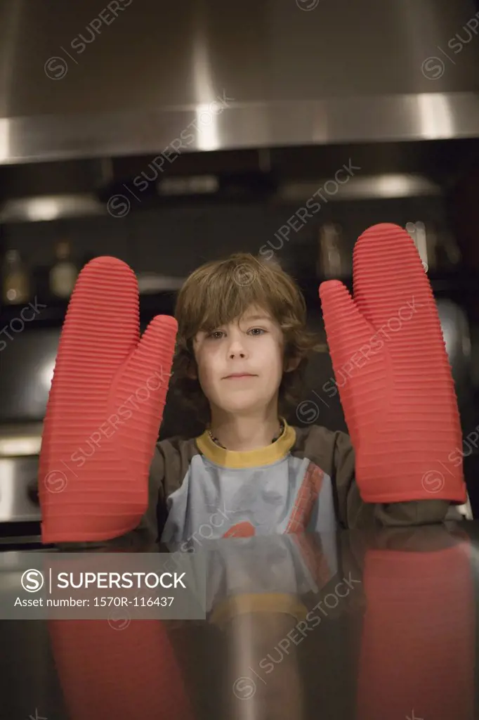 Young boy wearing large red oven mitts