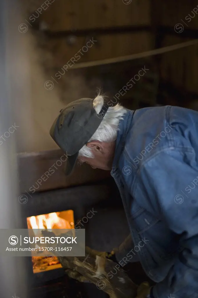 Senrior man putting wood into a furnace