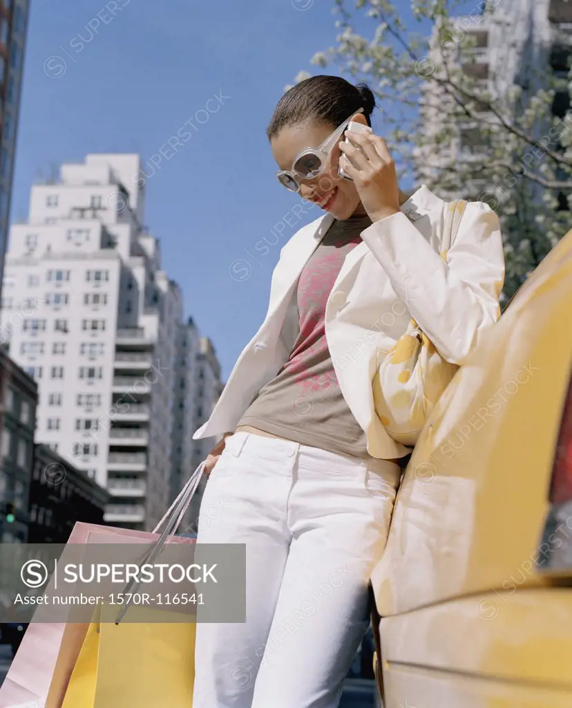 Woman leaning on a taxi whilst using a mobile phone and holding shopping bags