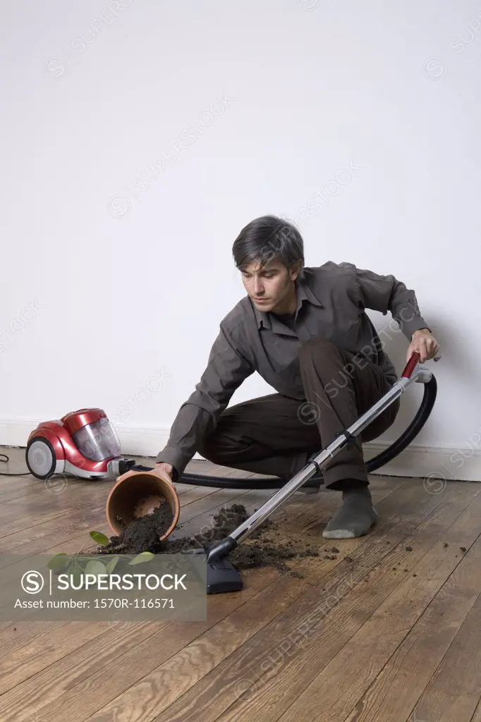 A man vacuuming up soil from a spilt potted plant