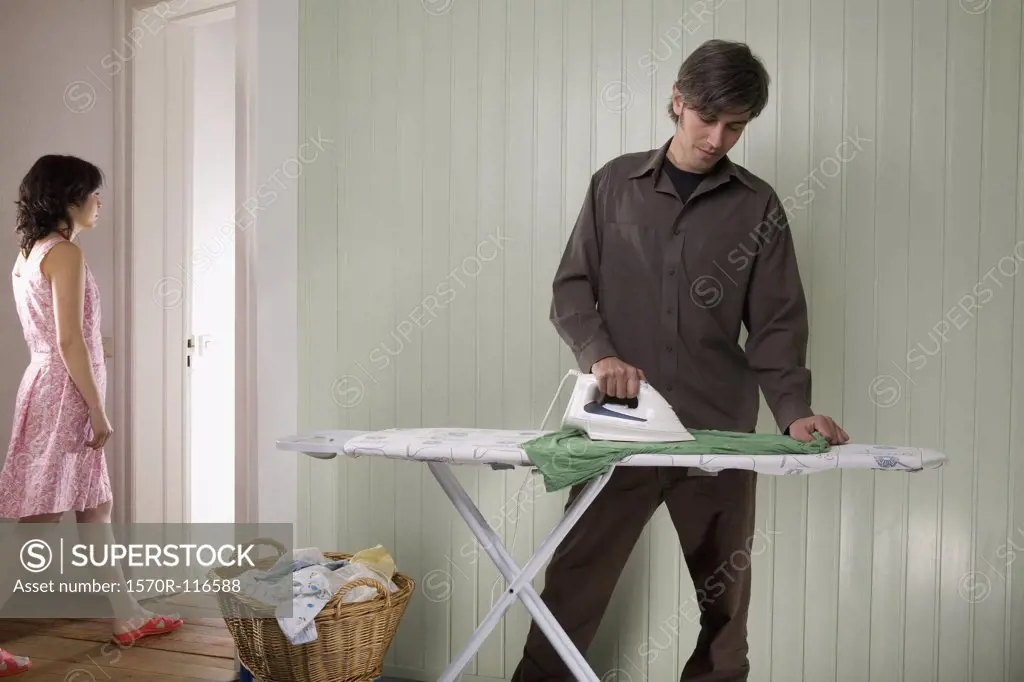 A man ironing whilst a woman is walking into another room