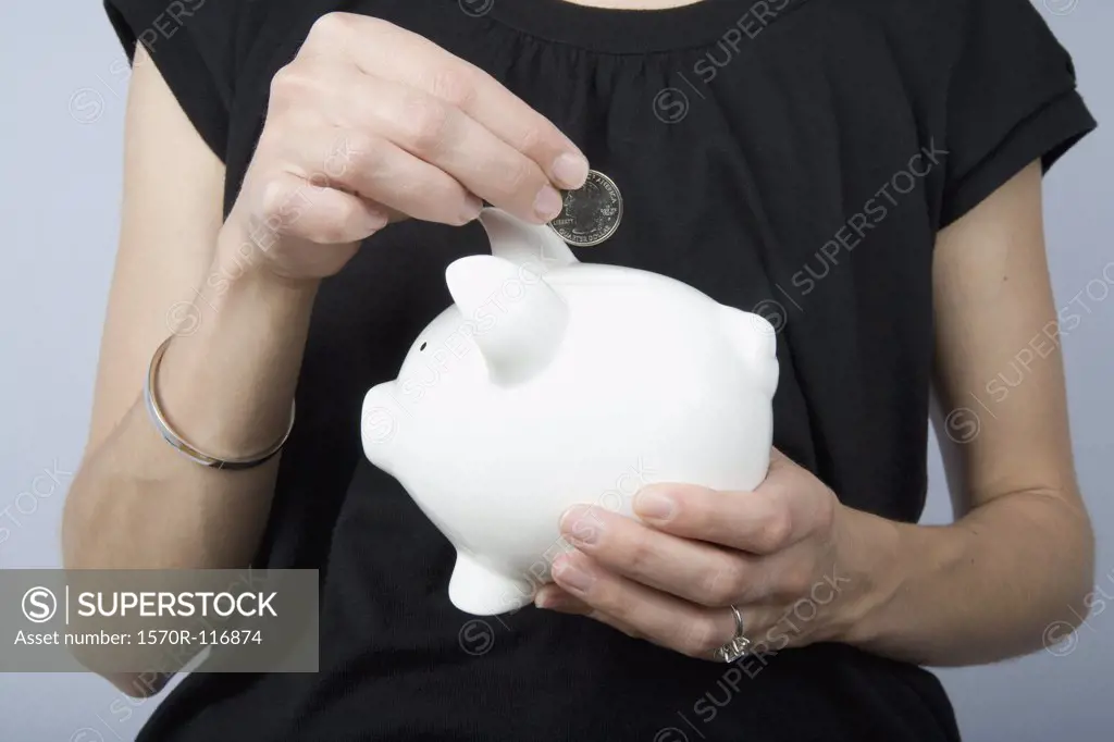 Detail of a woman holding a coin above a piggy bank