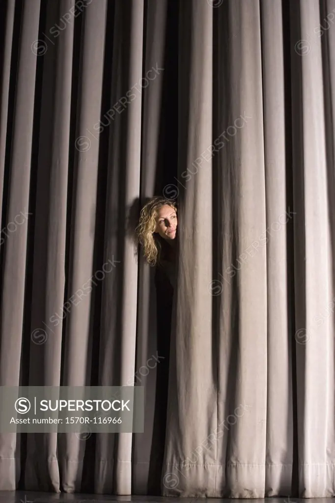 A woman peeking through a stage curtain