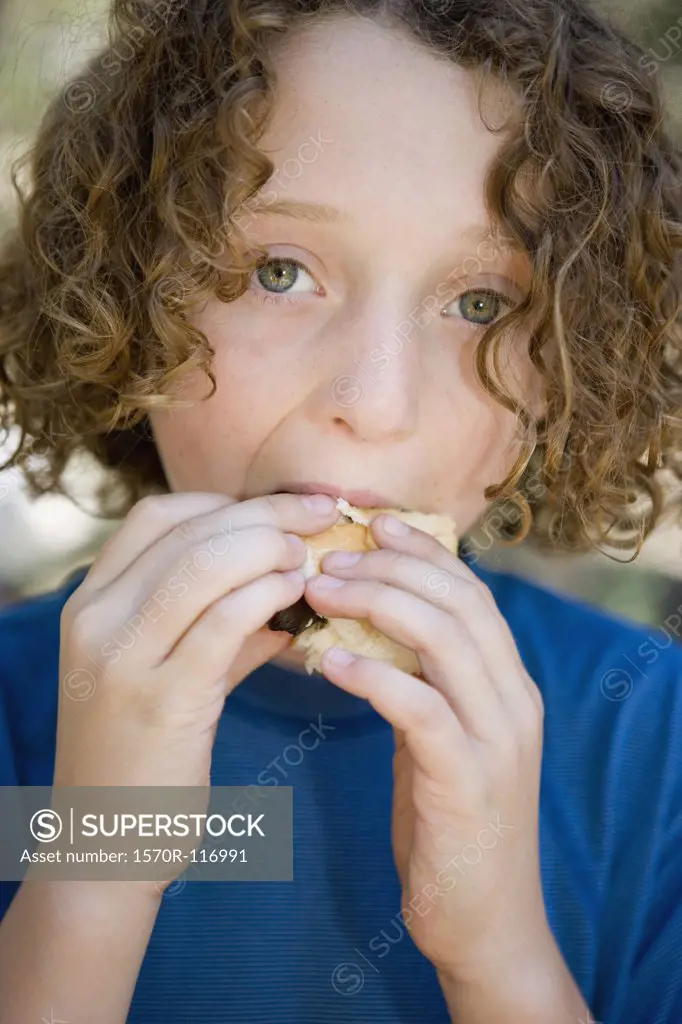 A young boy eating a sausage in a bread roll