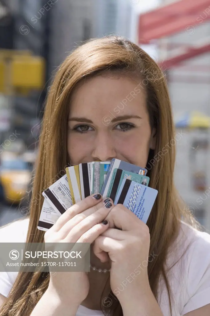 An adolescent girl holding a fan of credit cards over her mouth