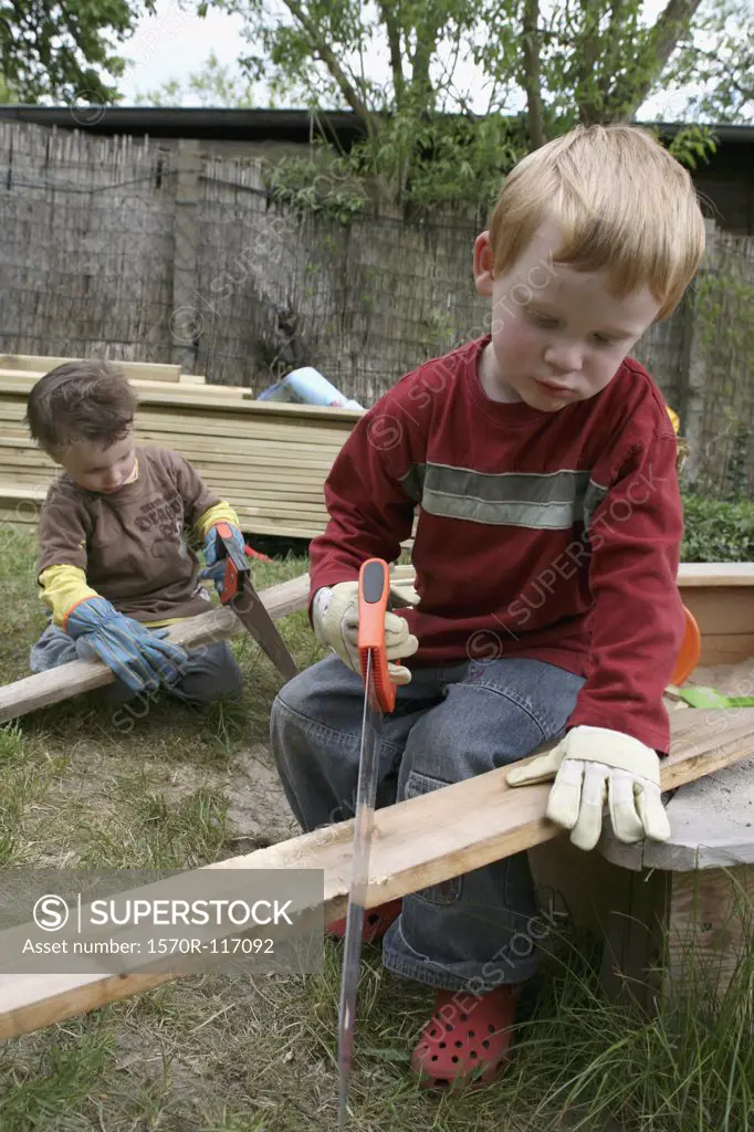 Two young boys sawing wood in a back yard
