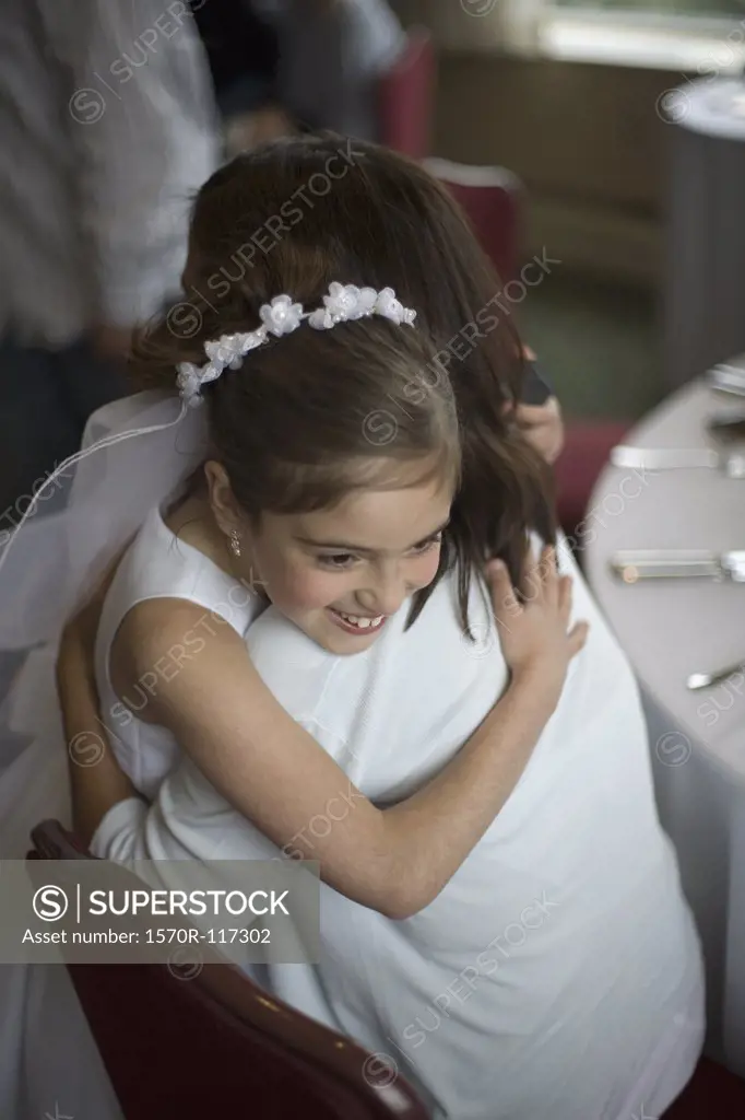 A young girl in her holy communion dress hugging her mother