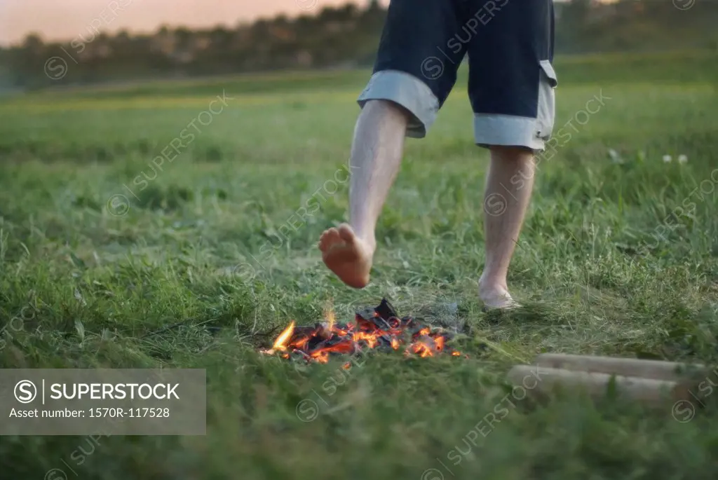 A man standing with his bare foot above a campfire