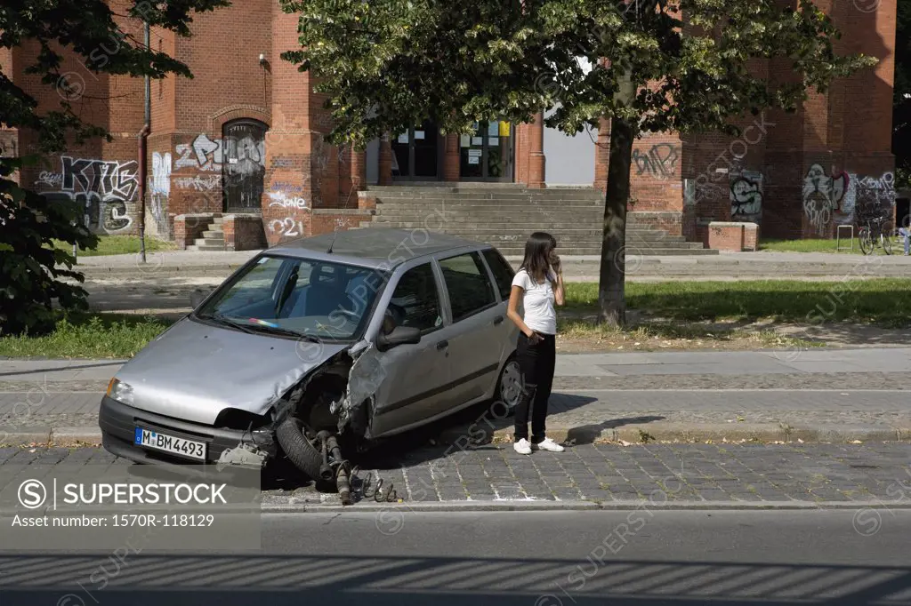 A young woman standing by damaged car