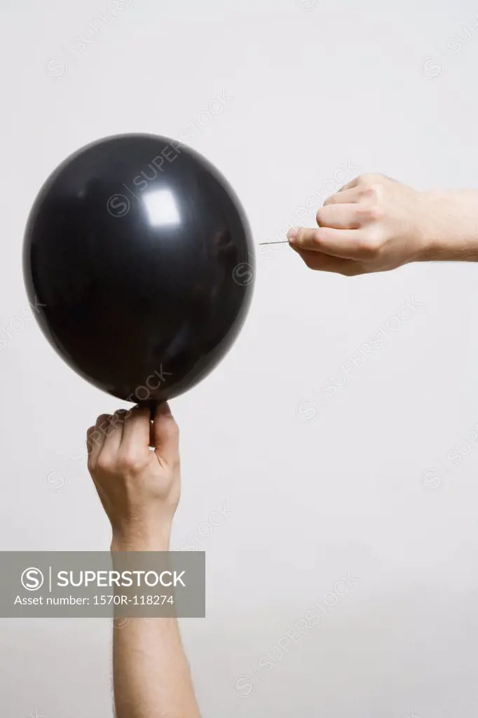 Detail of one person holding a balloon and another person holding a pin