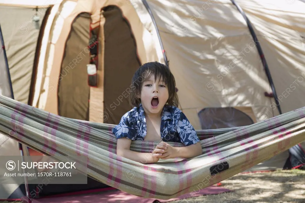 A boy sitting in a hammock and yawning