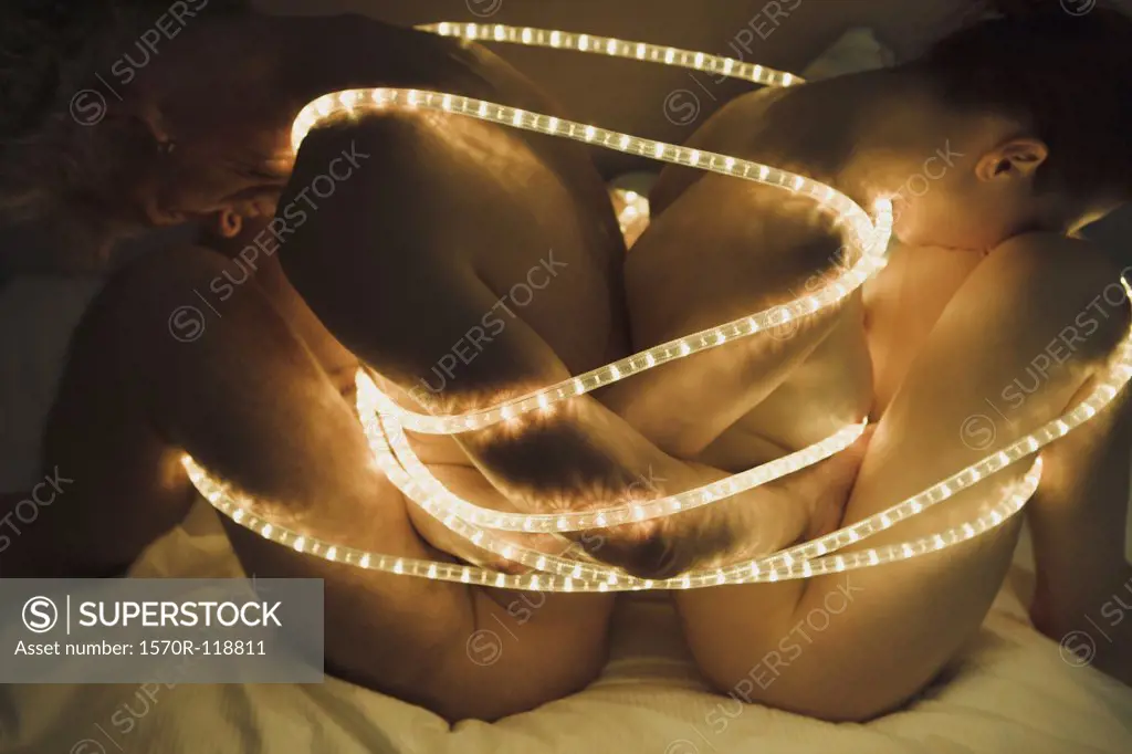 A naked man back to back with a naked woman wrapped up in twinkle lights