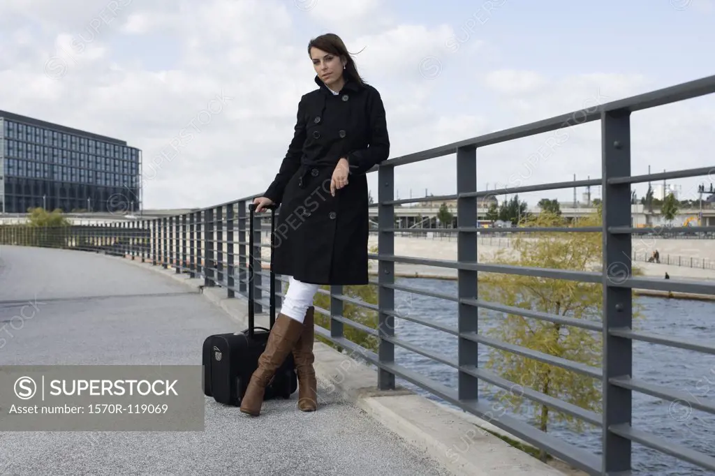 A woman standing on a bridge over a river with luggage