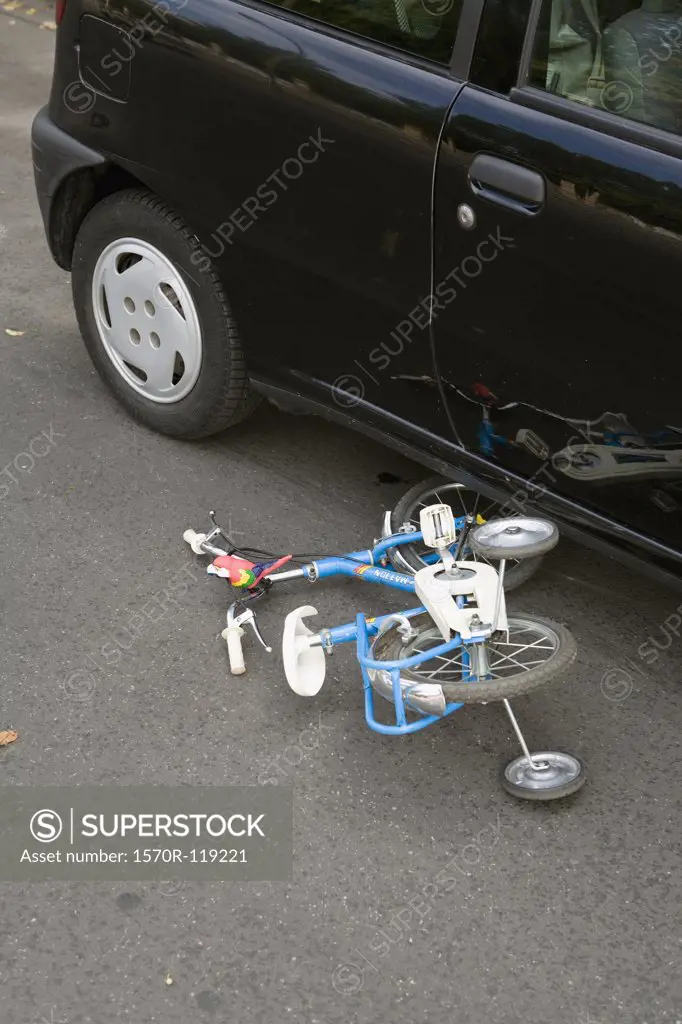 A child's bicycle lying on the road next to a car