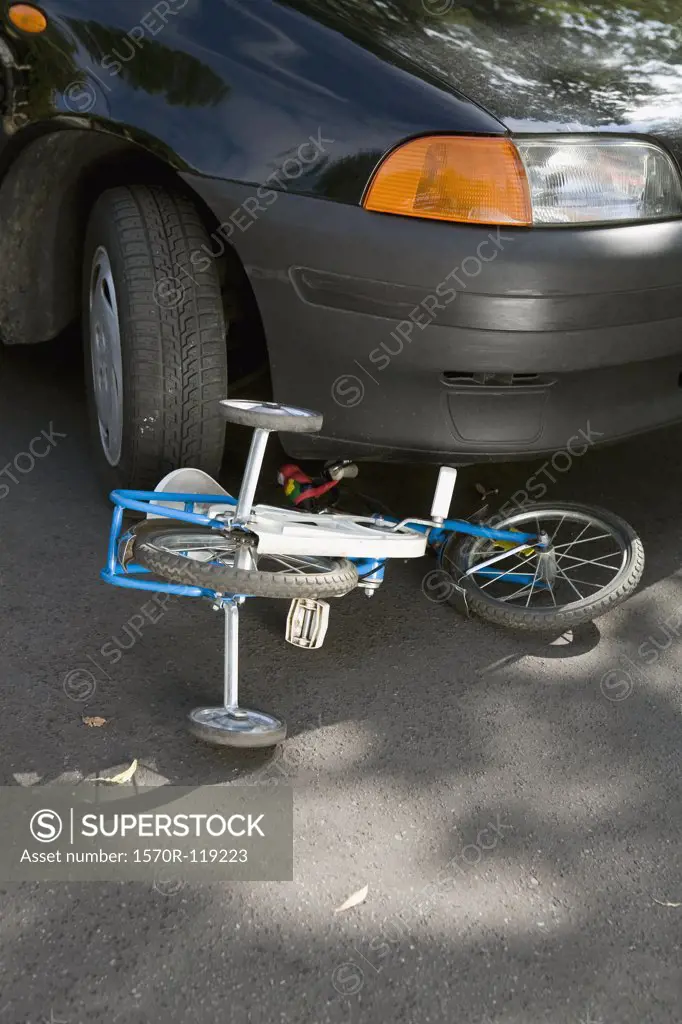 A child's bicycle lying on the road underneath a car