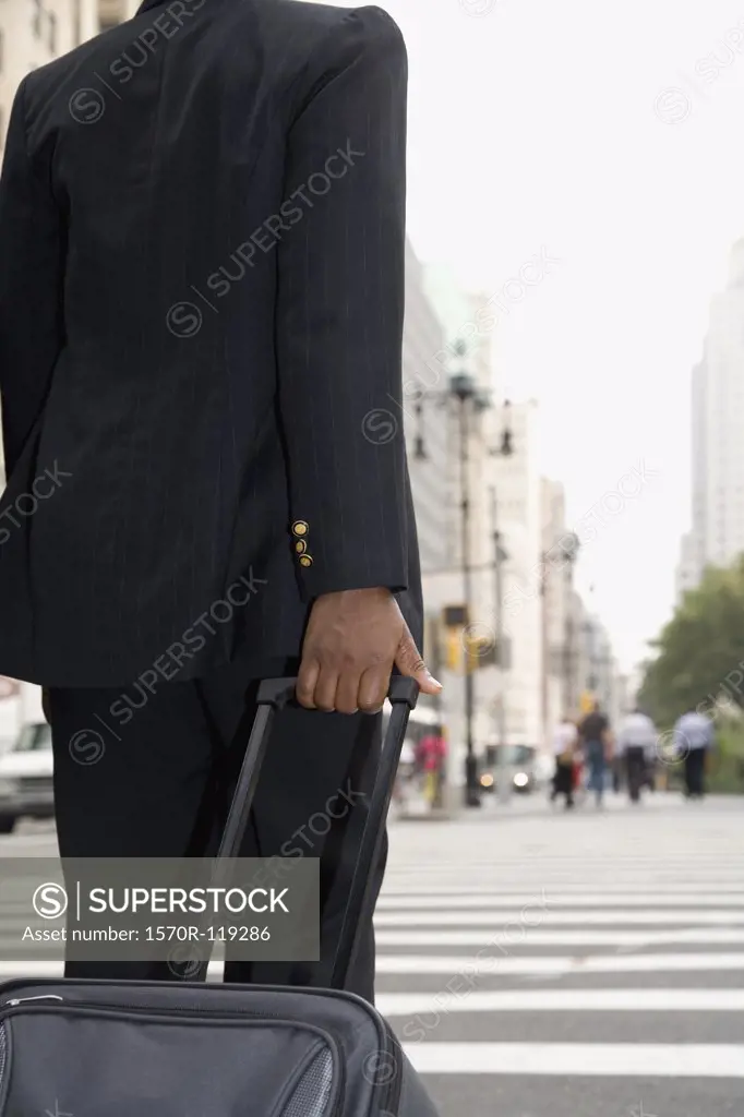 Businessperson rolling luggage down city street