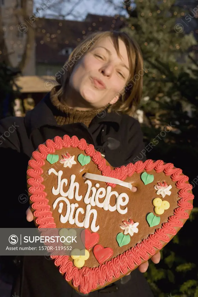 Woman holding a heart-shaped gingerbread cookie and puckering her lips