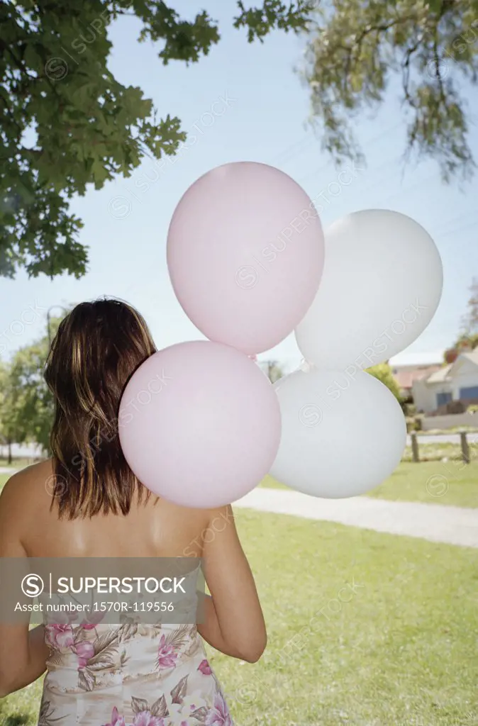 Woman standing in a park and holding a bunch of balloons