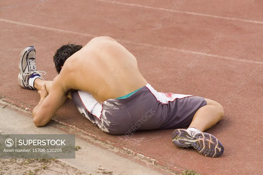 Male athlete stretching on the edge of a running track