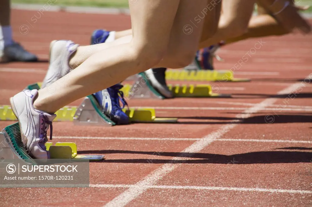 Female athletes with feet in starting blocks on a running track