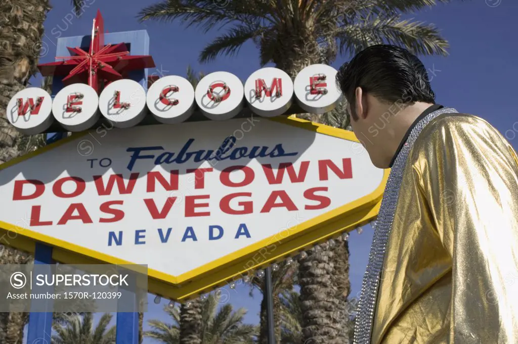Elvis impersonator standing below the ""Welcome to fabulous Las Vegas"" sign