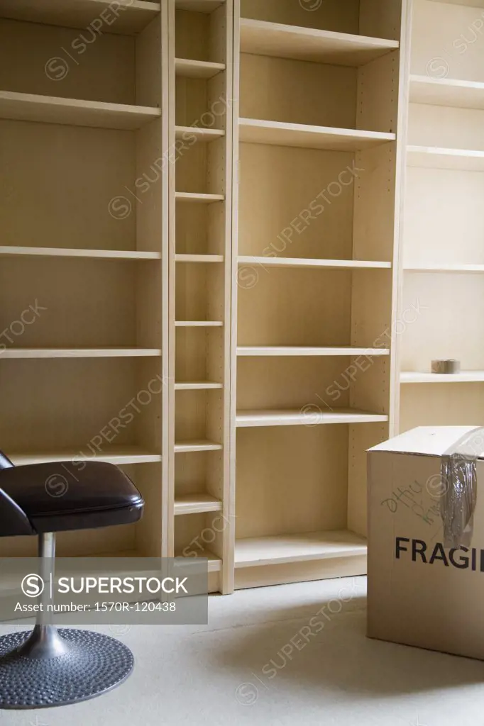 A chair and a cardboard box in front of empty bookshelves